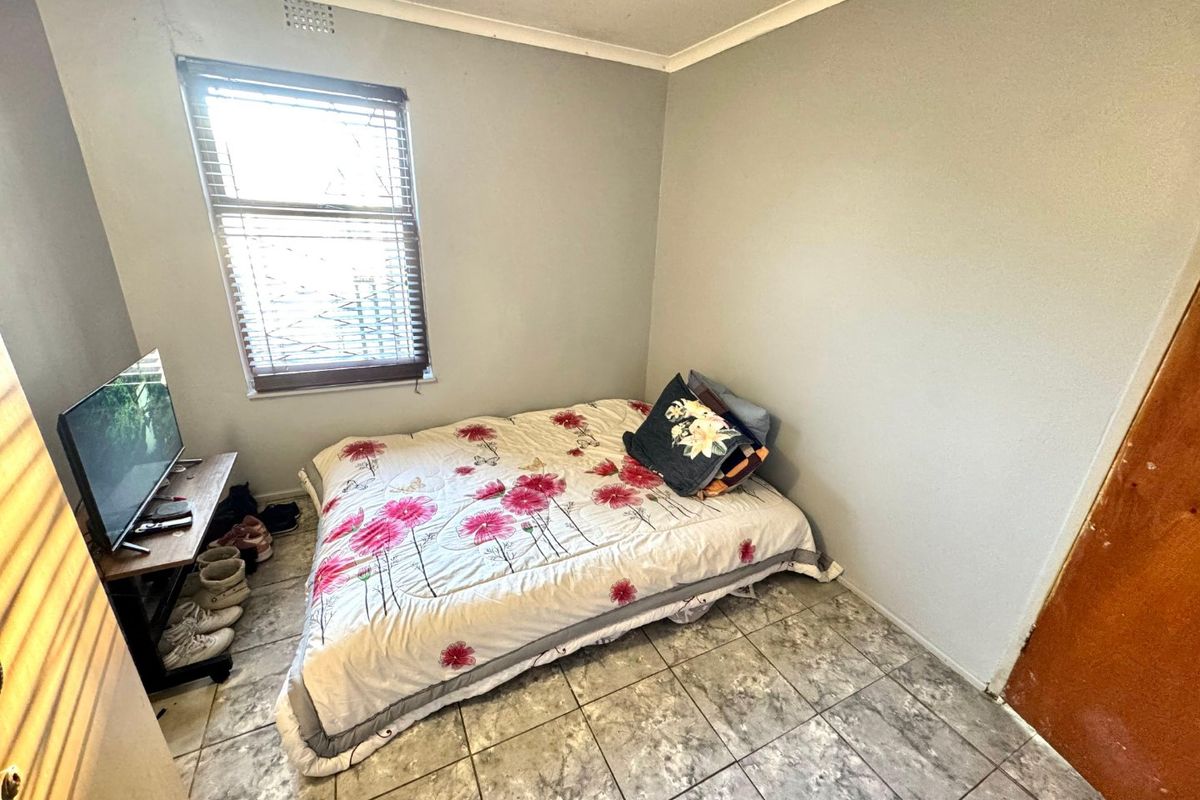 A compact bedroom featuring tiled flooring and a window with fitted blinds, requiring minor cosmetic updates to improve its overall appeal.