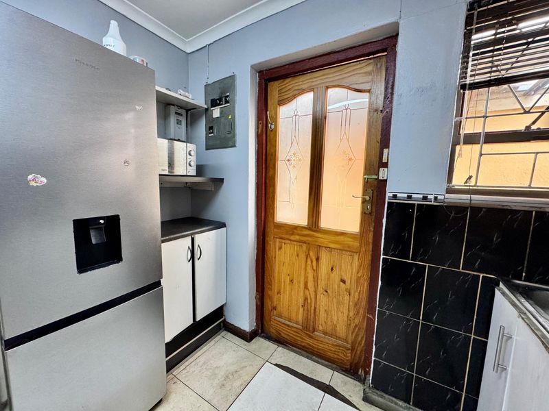 A functional scullery area featuring tiled flooring, built-in cabinetry, and a wooden door with decorative glass panels leading to the exterior.