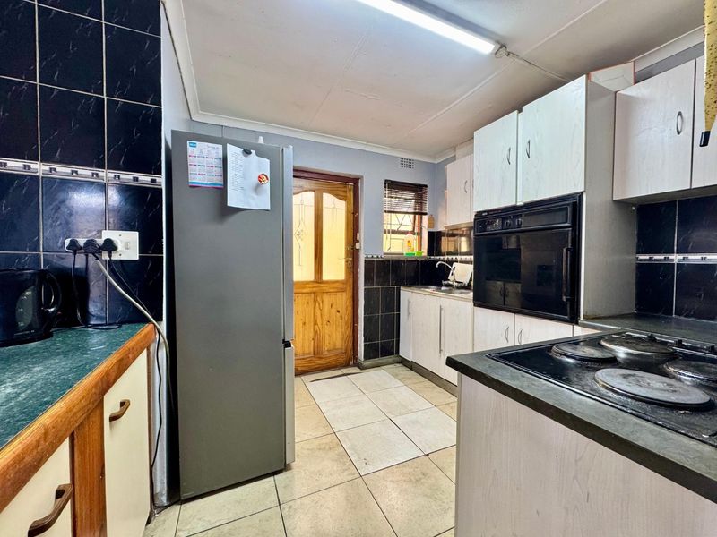 A functional kitchen featuring built-in cabinetry, an integrated oven, electric hob, and tiled surfaces, offering potential for modernization and aesthetic updates.
