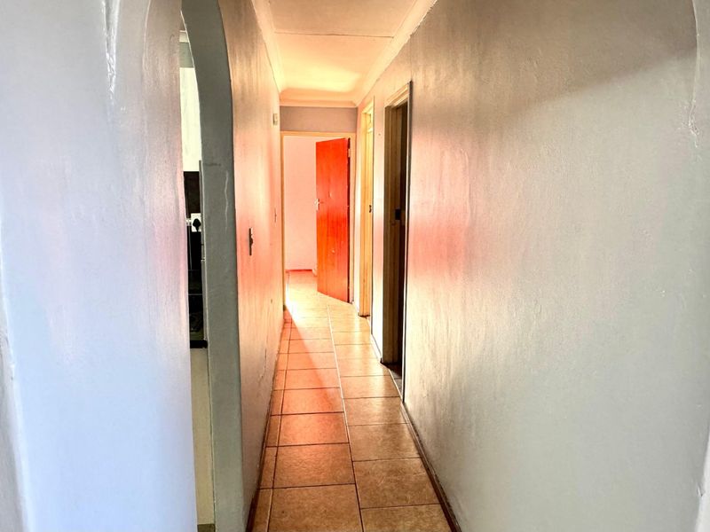 A narrow interior hallway featuring tiled flooring, coved ceilings, and an arched entryway leading to adjacent rooms.