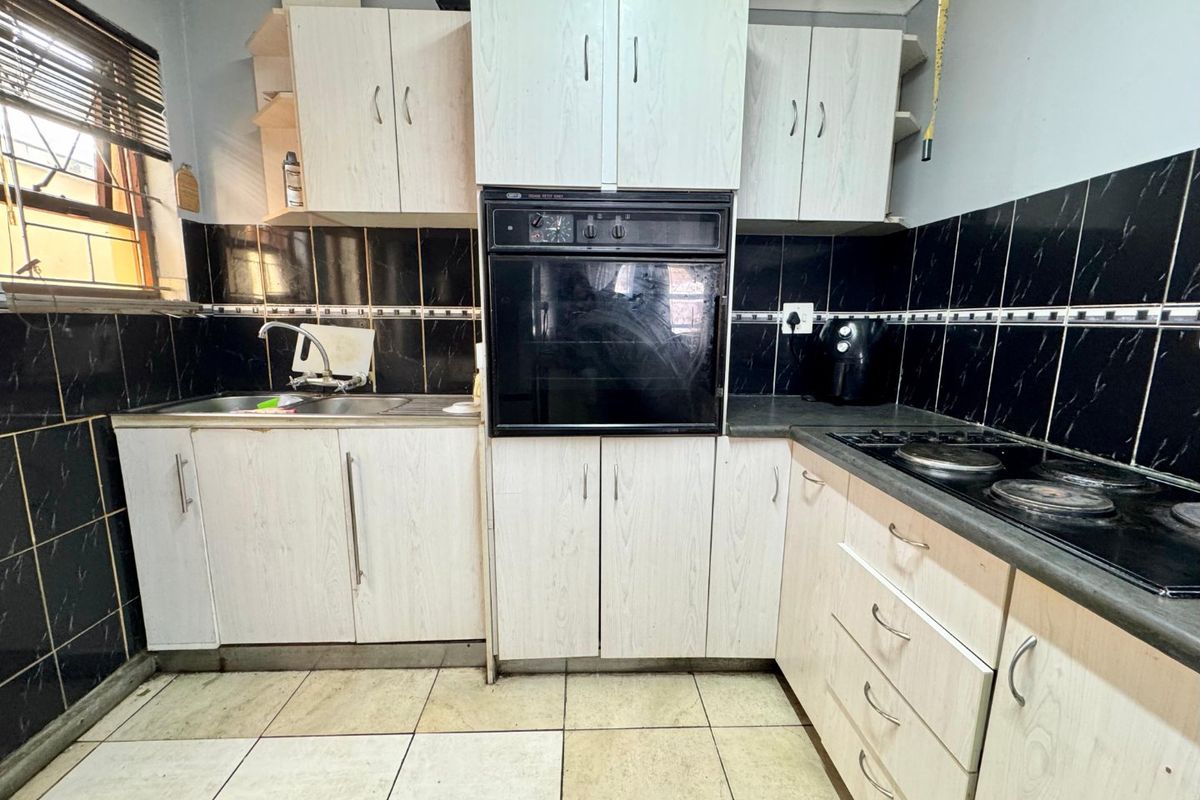 A functional kitchen featuring built-in cabinetry, an integrated oven, electric hob, and tiled finishes, offering potential for a modern renovation.