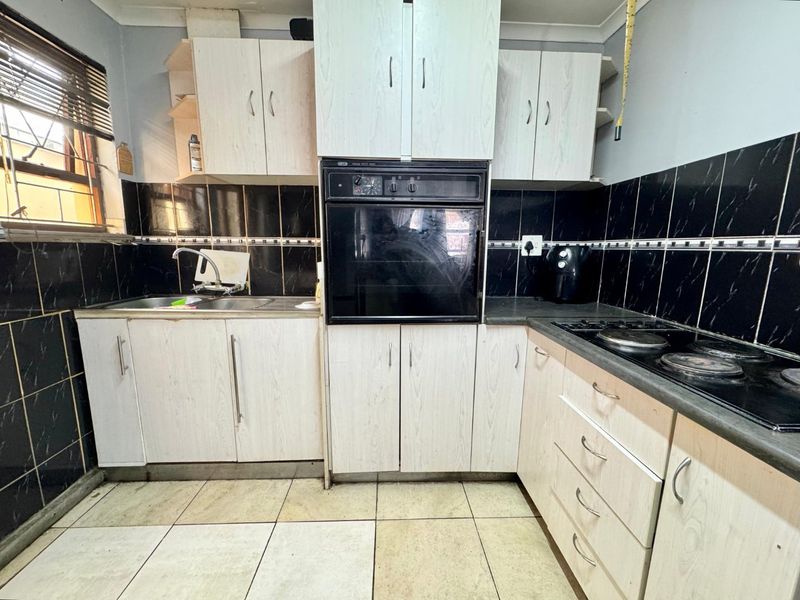 A functional kitchen featuring built-in cabinetry, an integrated oven, electric hob, and tiled finishes, offering potential for a modern renovation.