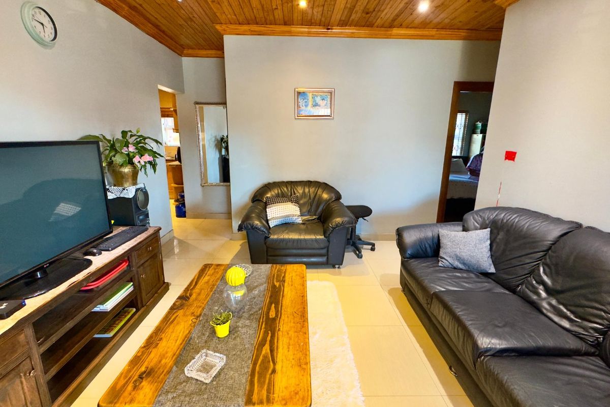 A living room featuring a timber tongue and groove ceiling, recessed downlights, and tiled flooring, providing a functional space with potential for modern updates.