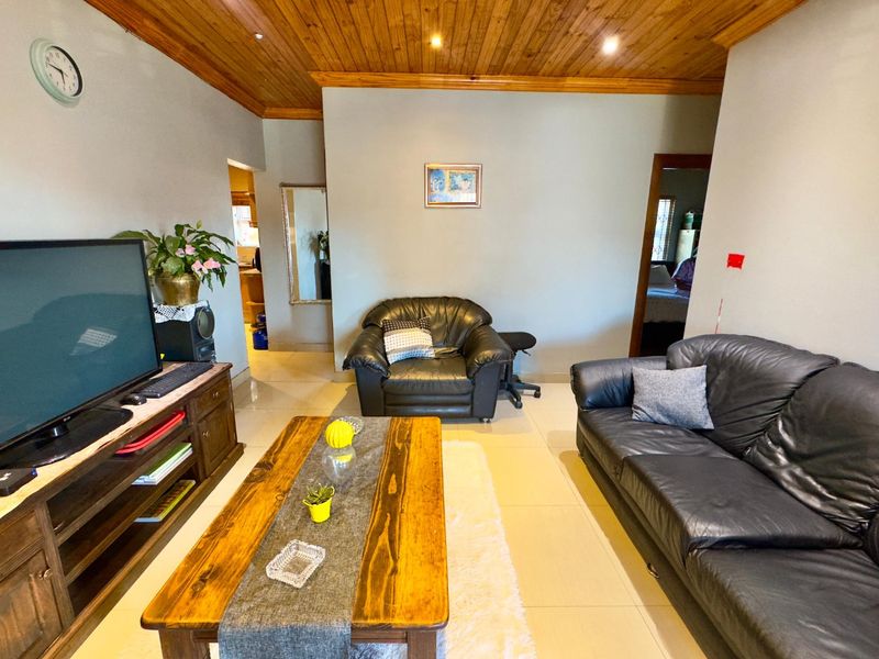 A living room featuring a timber tongue and groove ceiling, recessed downlights, and tiled flooring, providing a functional space with potential for modern updates.