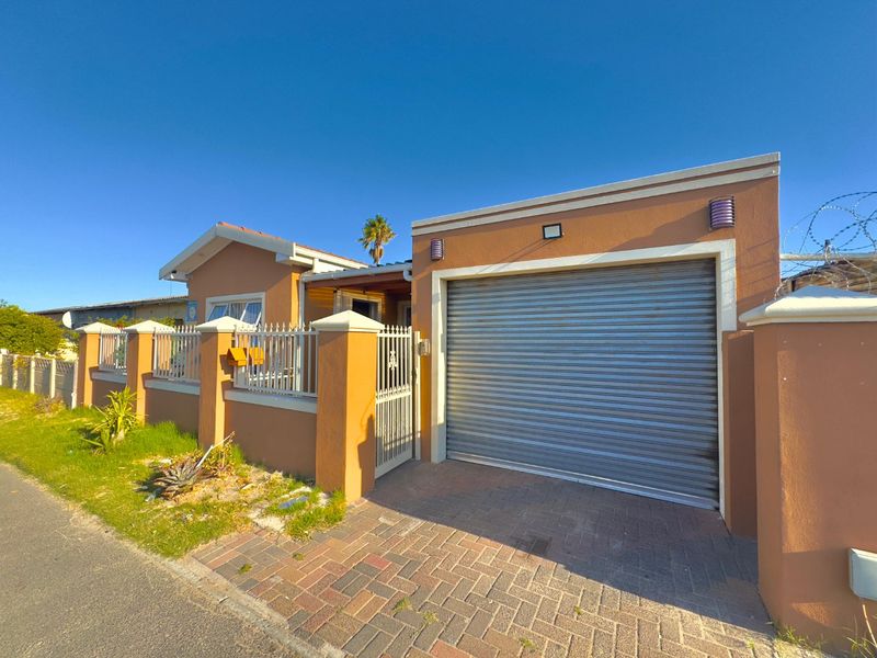 Front elevation of the property featuring a secure roller shutter garage door, paved driveway, and perimeter wall with integrated security fencing.