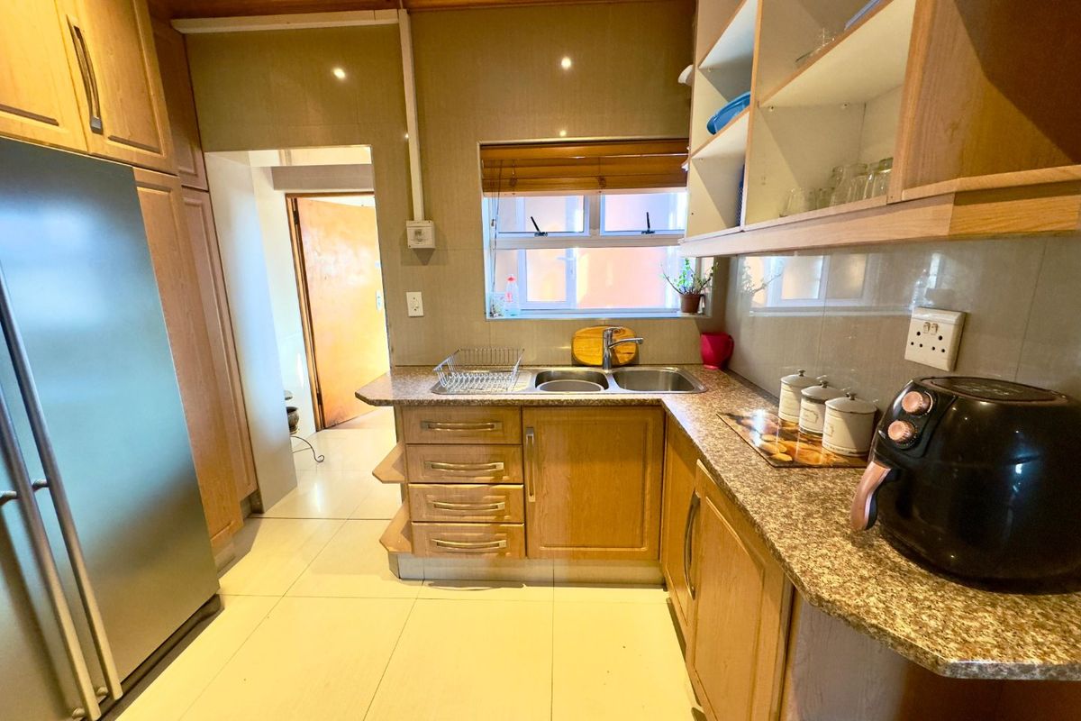 A functional kitchen featuring wooden cabinetry, granite countertops, a double basin sink, and tiled flooring with a warm wooden ceiling finish.