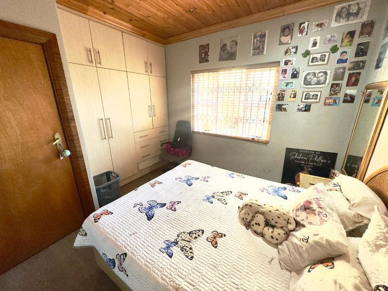 A bedroom featuring built-in cupboards, a timber ceiling, and a window fitted with security bars and venetian blinds.