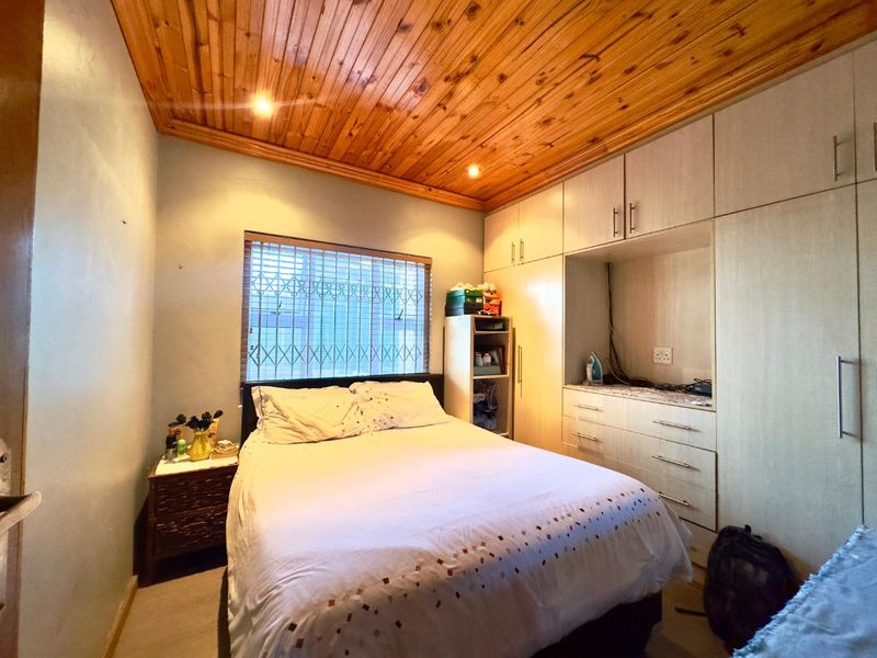 A bedroom featuring built-in cupboards, a timber-clad ceiling with recessed lighting, and security bars on the window.