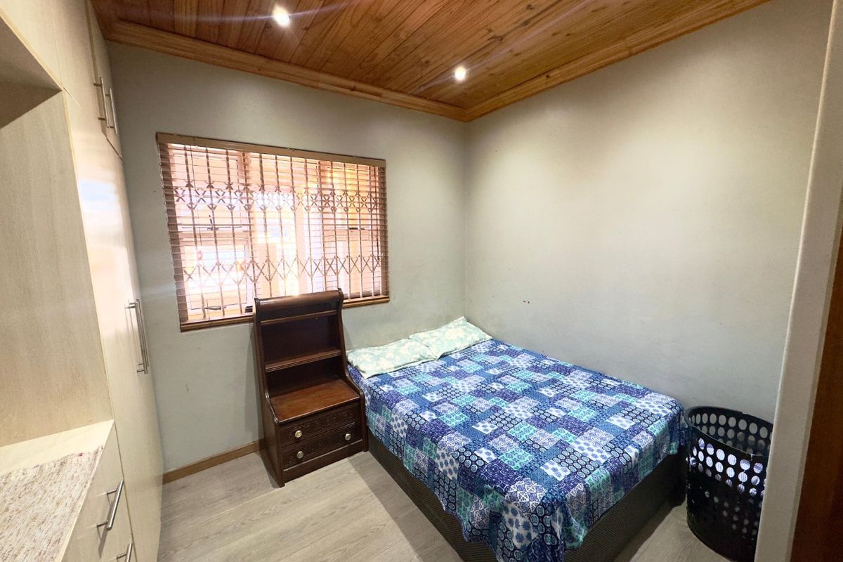 A compact bedroom featuring built-in cupboards, laminate flooring, and a timber-clad ceiling with recessed lighting.