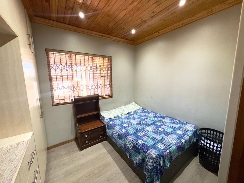 A compact bedroom featuring built-in cupboards, laminate flooring, and a timber-clad ceiling with recessed lighting.