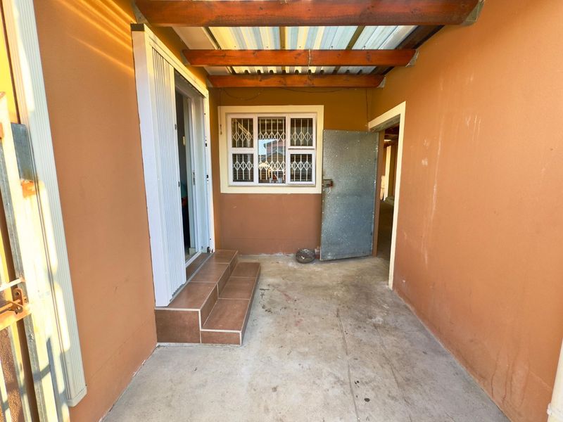 A covered outdoor patio area featuring tiled steps, security fixtures, and a timber pergola structure, providing a functional transition space.