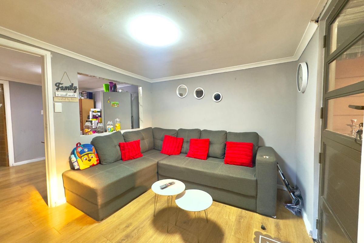 A cozy living room featuring laminate flooring, a coved ceiling, and a convenient pass-through window connecting to the kitchen area.