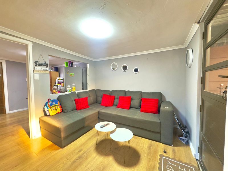 A cozy living room featuring laminate flooring, a coved ceiling, and a convenient pass-through window connecting to the kitchen area.