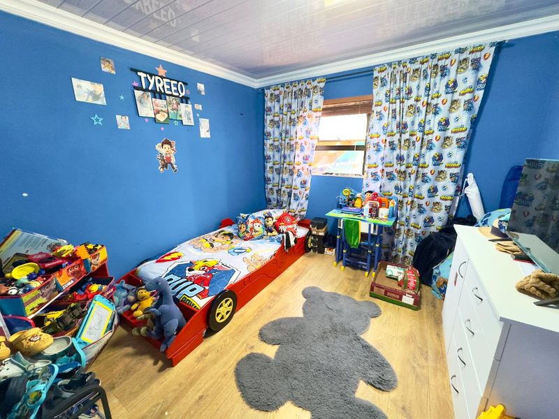A bedroom featuring laminate flooring and a coved ceiling, currently utilized as a child's room with blue painted walls.