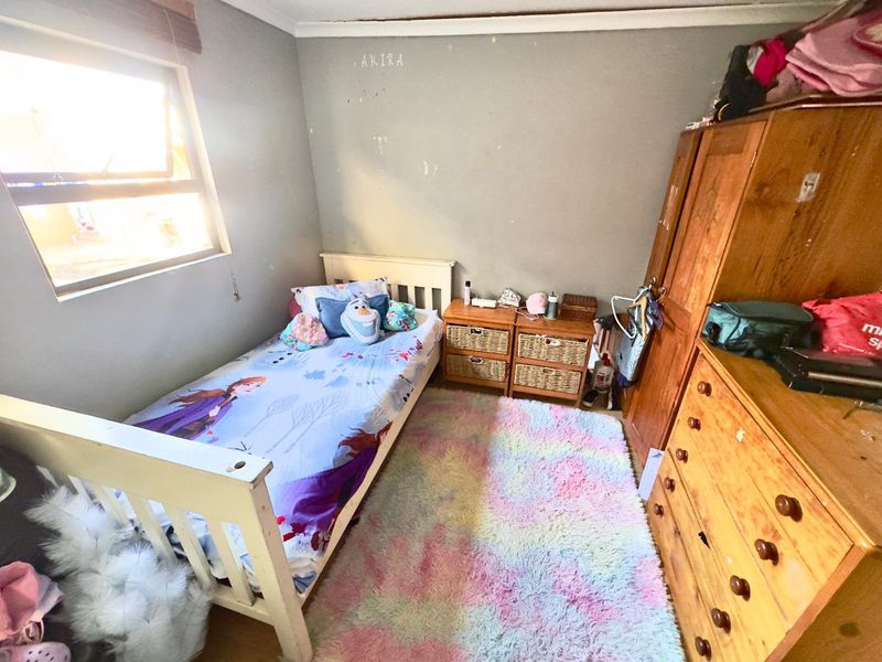 A bedroom featuring timber flooring and a top-hung window, currently requiring cosmetic updates to the wall finishes.
