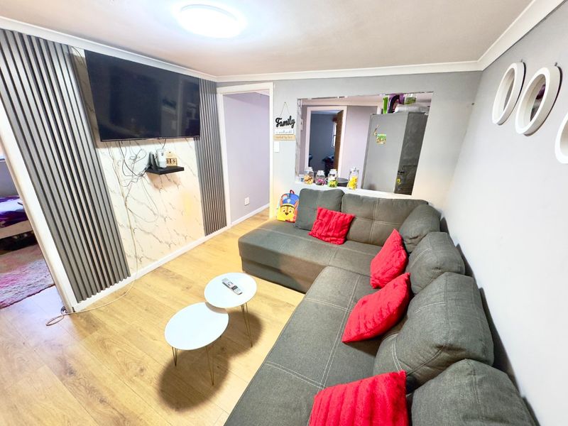 Living room featuring laminate flooring, decorative wall paneling, and a convenient pass-through window connecting to the kitchen area.