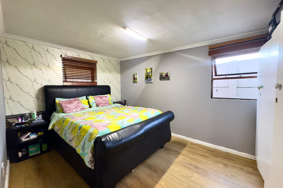 A bedroom featuring laminate flooring, built-in wardrobe storage, and dual windows with venetian blinds.