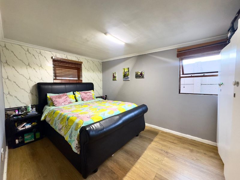 A bedroom featuring laminate flooring, built-in wardrobe storage, and dual windows with venetian blinds.