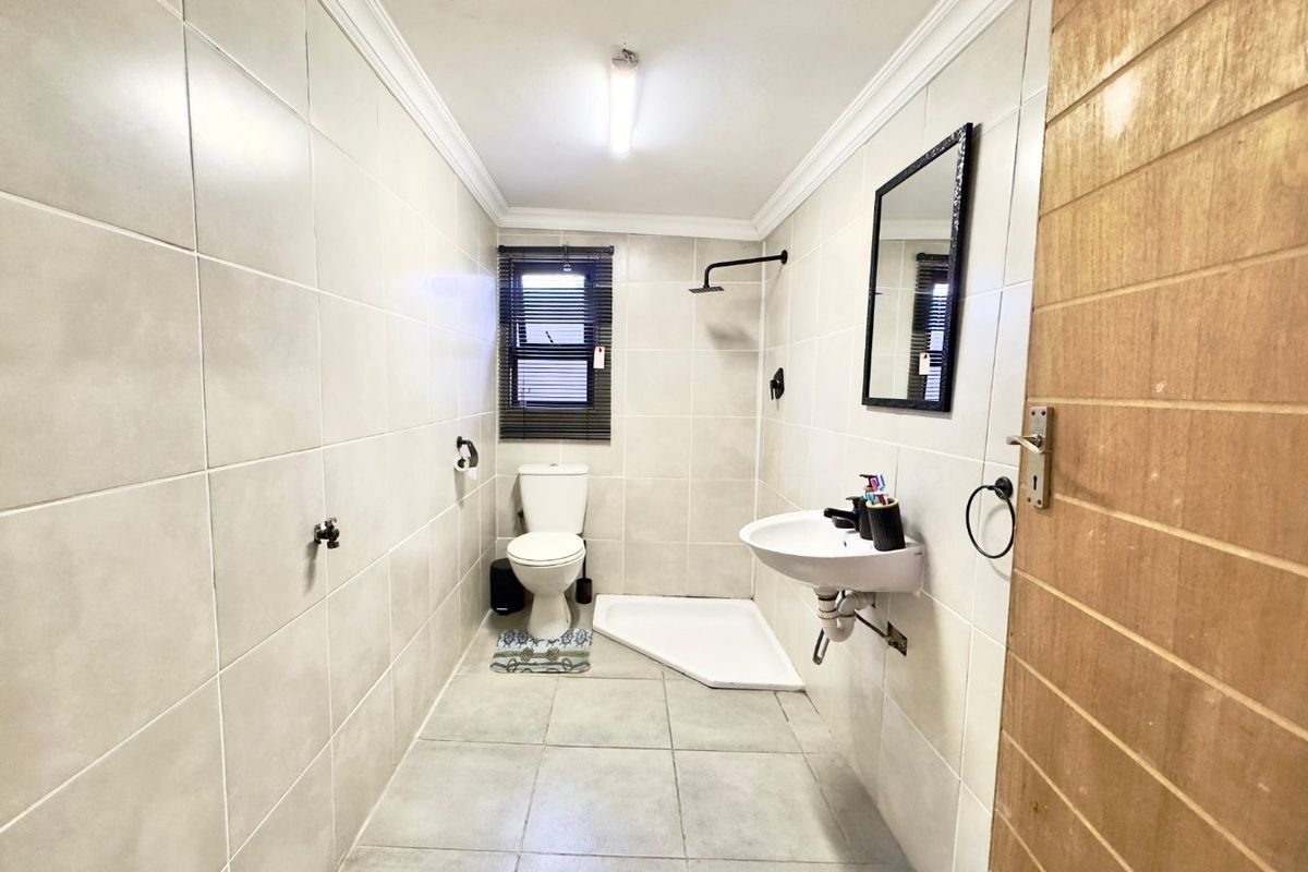 A clean, functional bathroom featuring tiled walls and flooring, a pedestal washbasin, a toilet, and a walk-in shower area.
