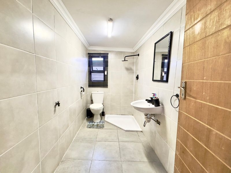 A clean, functional bathroom featuring tiled walls and flooring, a pedestal washbasin, a toilet, and a walk-in shower area.