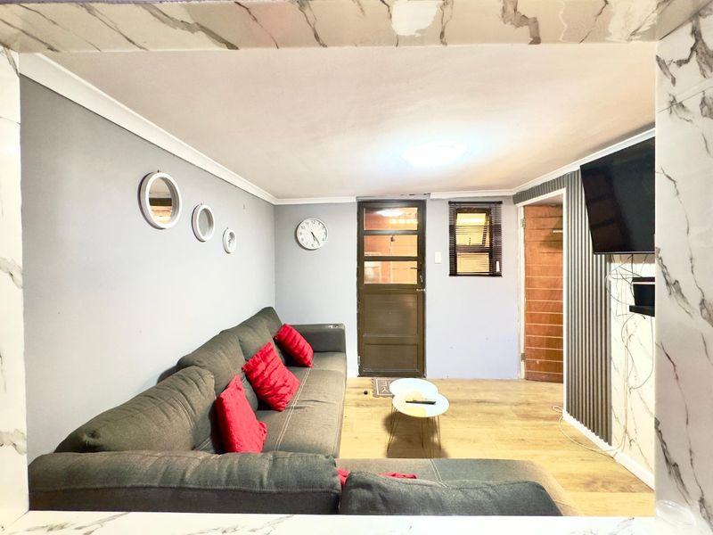 A living room featuring laminate flooring, coving, and a timber door, with wall-mounted television infrastructure and neutral grey wall tones.