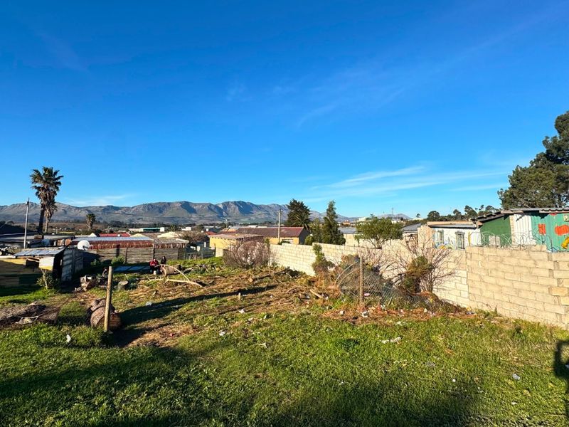A vacant residential plot featuring a perimeter boundary wall with razor wire, offering mountain views in a suburban setting.