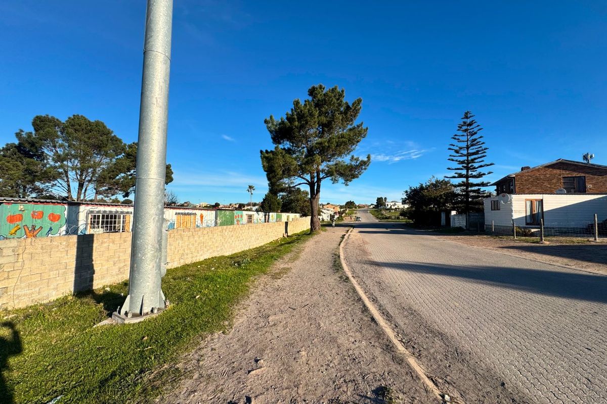 A street view showing a paved road, grass verge, and a concrete block boundary wall in a residential neighborhood.