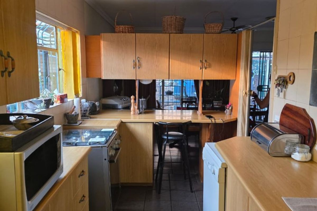 A functional kitchen featuring laminate cabinetry, tiled splashbacks, and a convenient breakfast bar area, offering a practical layout with potential for modern updates.
