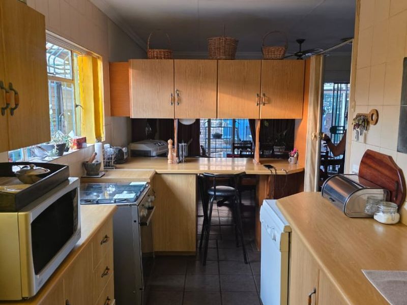 A functional kitchen featuring laminate cabinetry, tiled splashbacks, and a convenient breakfast bar area, offering a practical layout with potential for modern updates.