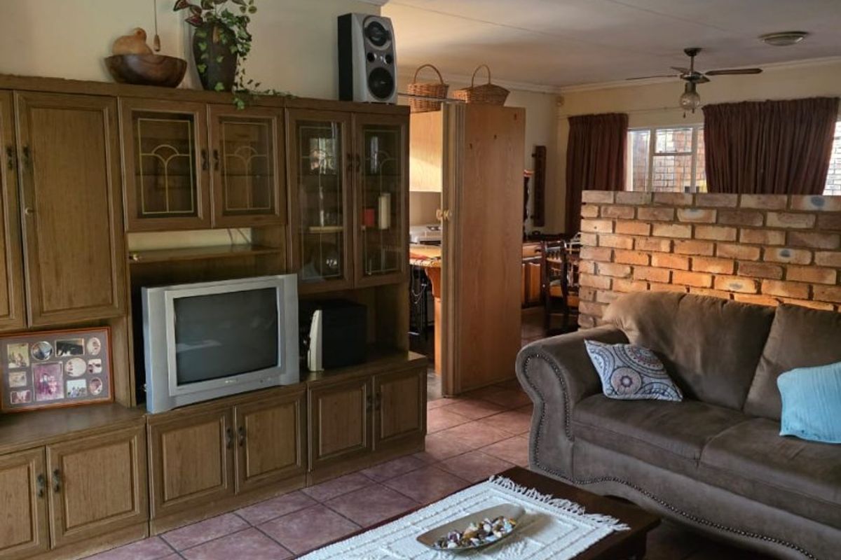 A living room featuring ceramic tile flooring, a ceiling fan, and a decorative exposed brick partition wall separating the space from the kitchen area.