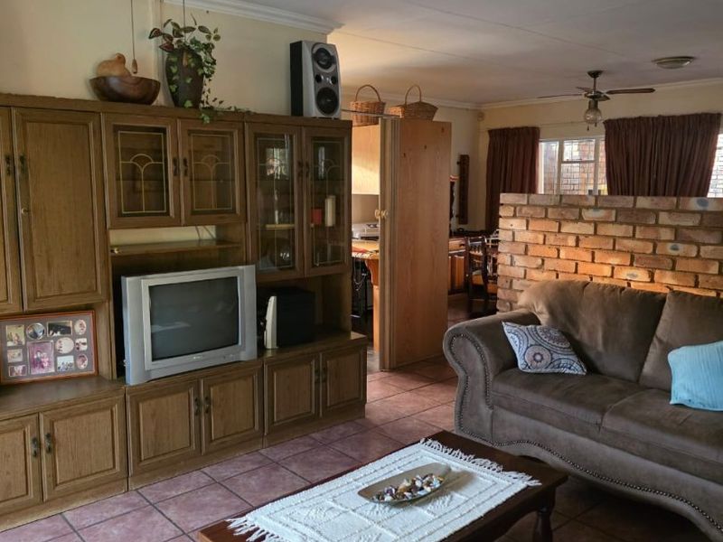 A living room featuring ceramic tile flooring, a ceiling fan, and a decorative exposed brick partition wall separating the space from the kitchen area.