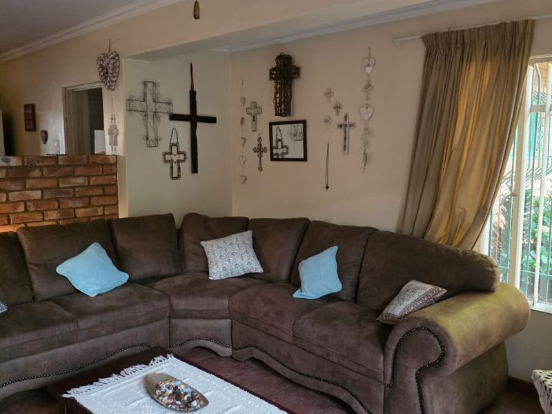 A cozy living room featuring tiled flooring, an exposed brick accent wall, and a ceiling fan, offering a comfortable and traditional living space.
