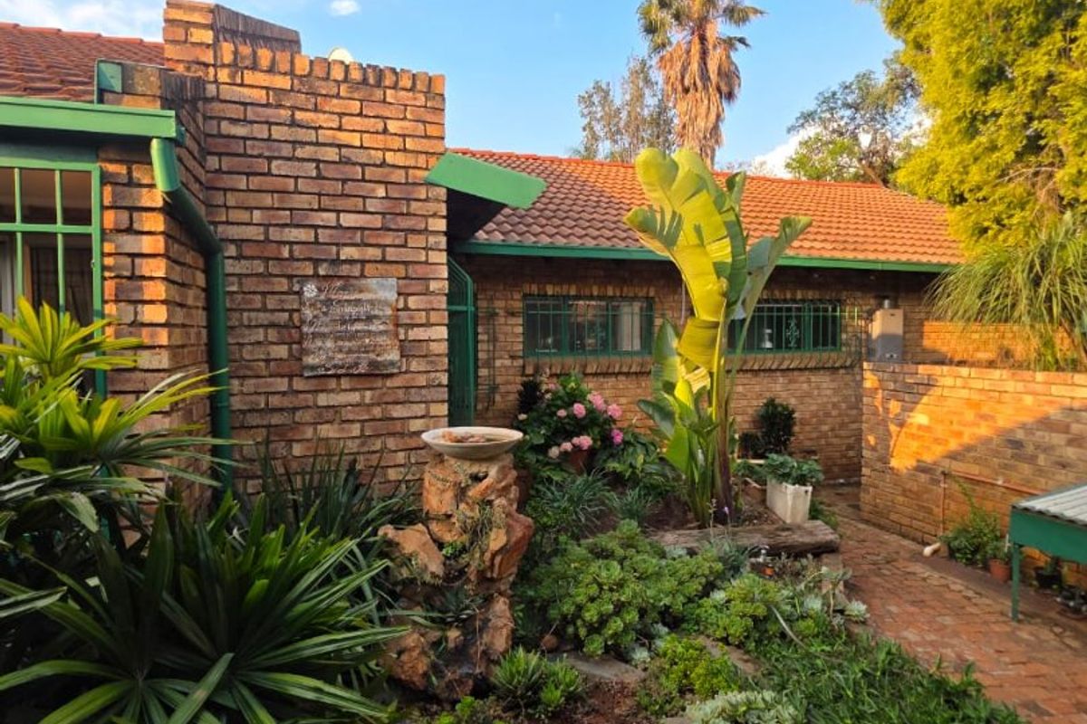 A well-maintained rear garden area featuring established landscaping, brick paving, and a classic brick facade with tiled roofing.