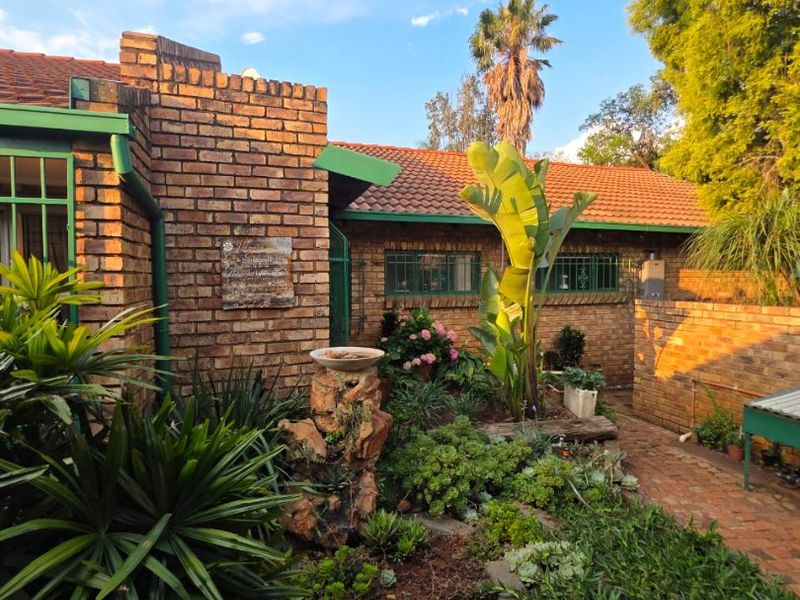 A well-maintained rear garden area featuring established landscaping, brick paving, and a classic brick facade with tiled roofing.