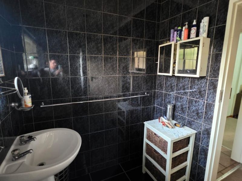 A bathroom featuring dark wall and floor tiles, a white pedestal basin, and a wall-mounted medicine cabinet.