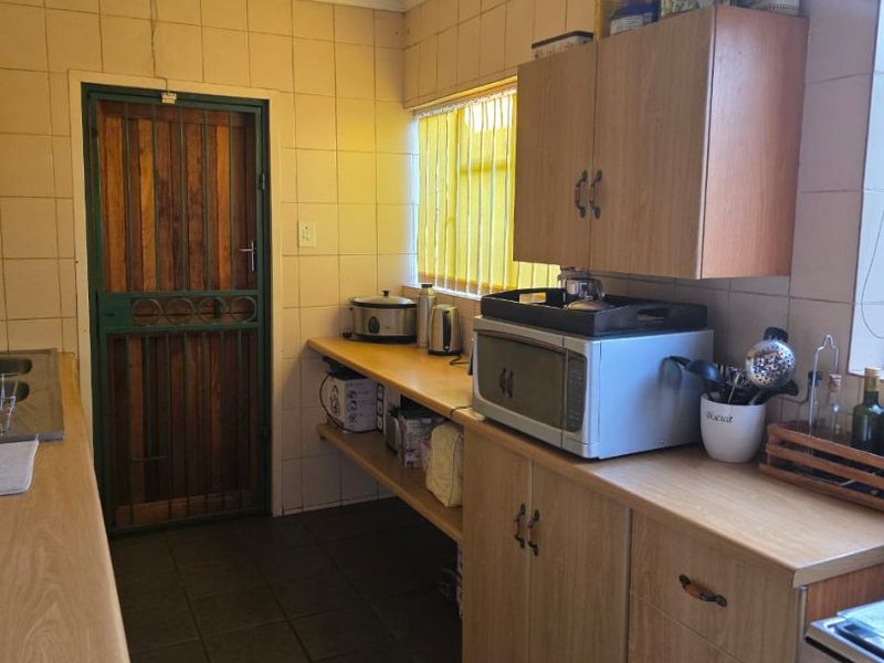 A functional kitchen featuring laminate countertops, built-in cabinetry, tiled walls, and tiled flooring, with a security gate leading to the exterior.