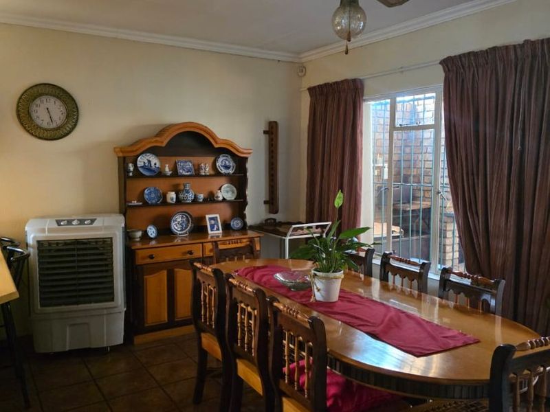 A functional dining room featuring tiled flooring, a ceiling fan, and large windows with security bars, providing a practical space for family meals.