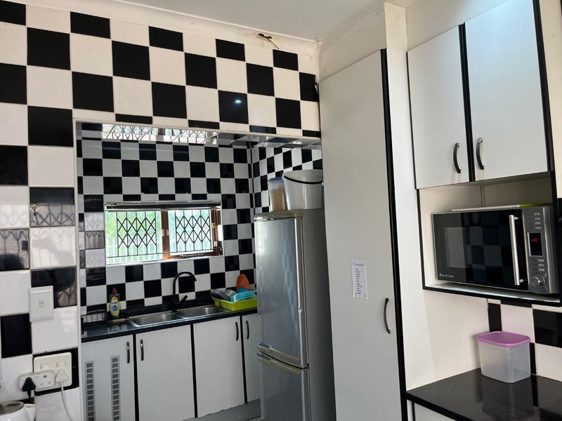 A functional kitchen featuring black and white checkered wall tiles, built-in cabinetry, a double sink, and integrated microwave space.