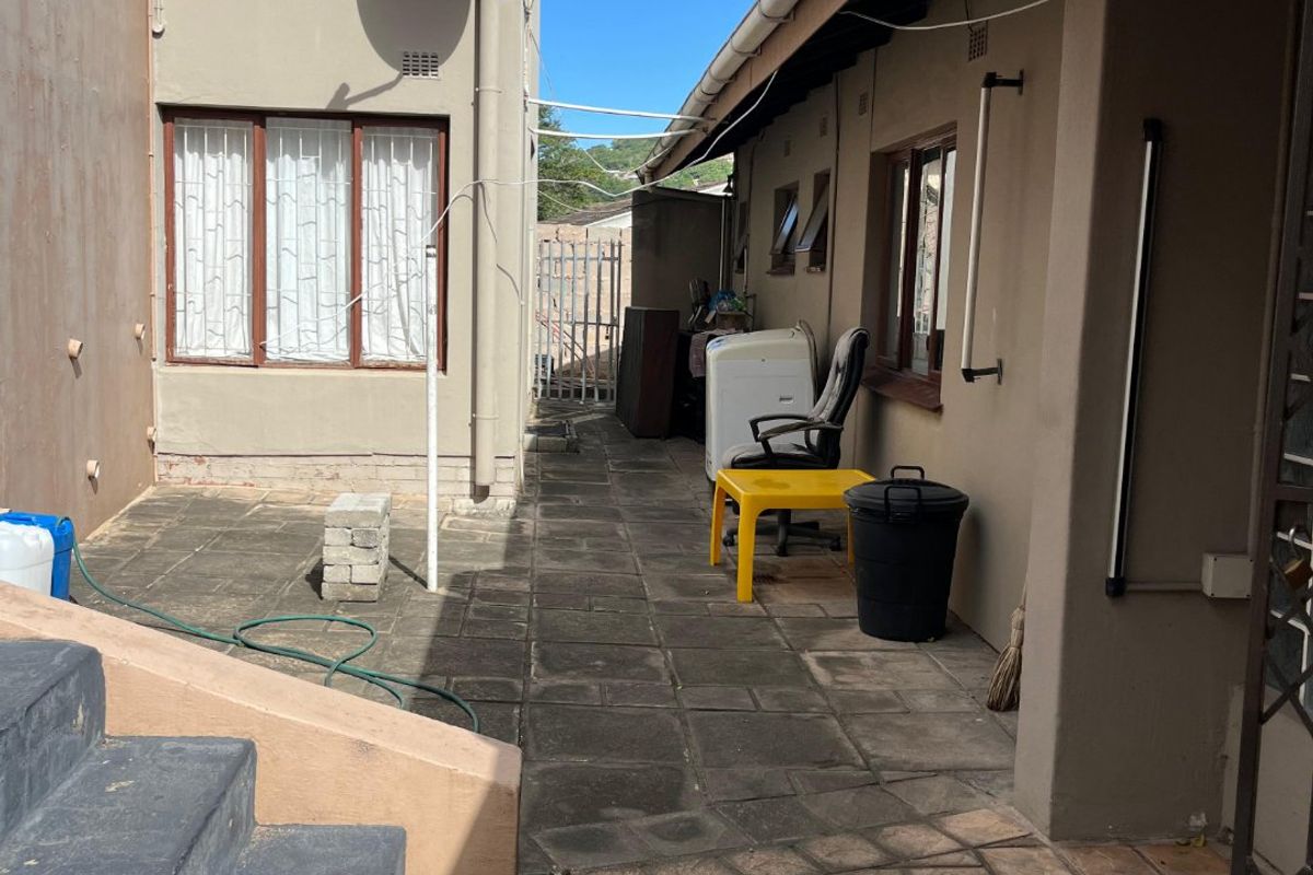 A paved rear courtyard area featuring concrete stairs, exterior wall access, and basic utility infrastructure.