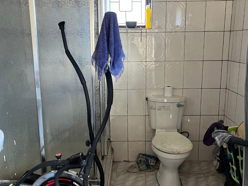 A functional bathroom featuring a shower enclosure, toilet, and tiled finishes, currently requiring maintenance and cosmetic updates.