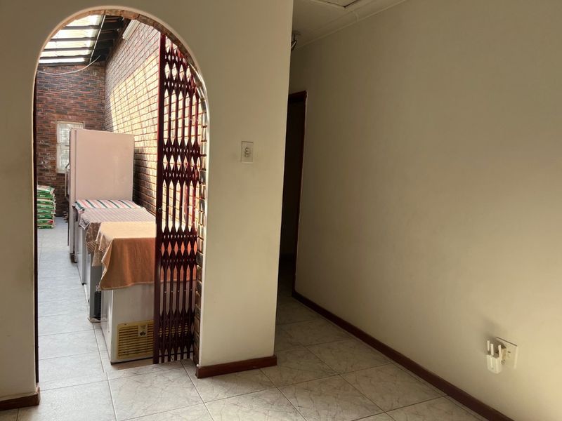 A functional scullery area featuring an arched entrance, exposed brickwork, tiled flooring, and a skylight providing natural light.