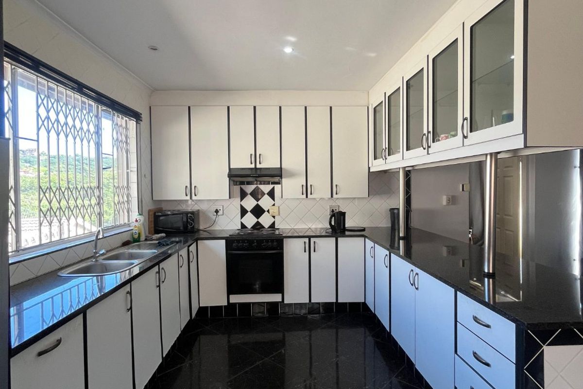 A well-maintained kitchen featuring black granite countertops, white cabinetry with dark trim, built-in oven, extractor fan, and polished black floor tiles.