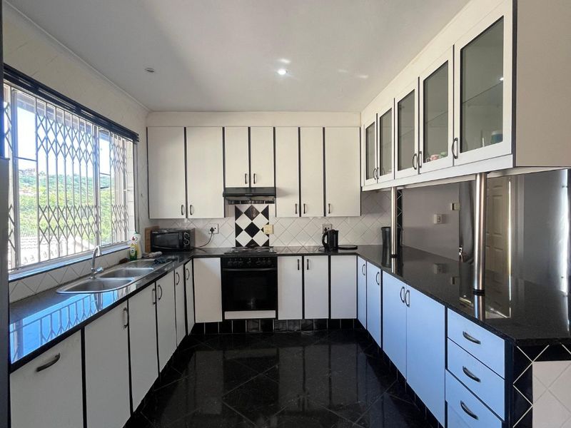 A well-maintained kitchen featuring black granite countertops, white cabinetry with dark trim, built-in oven, extractor fan, and polished black floor tiles.