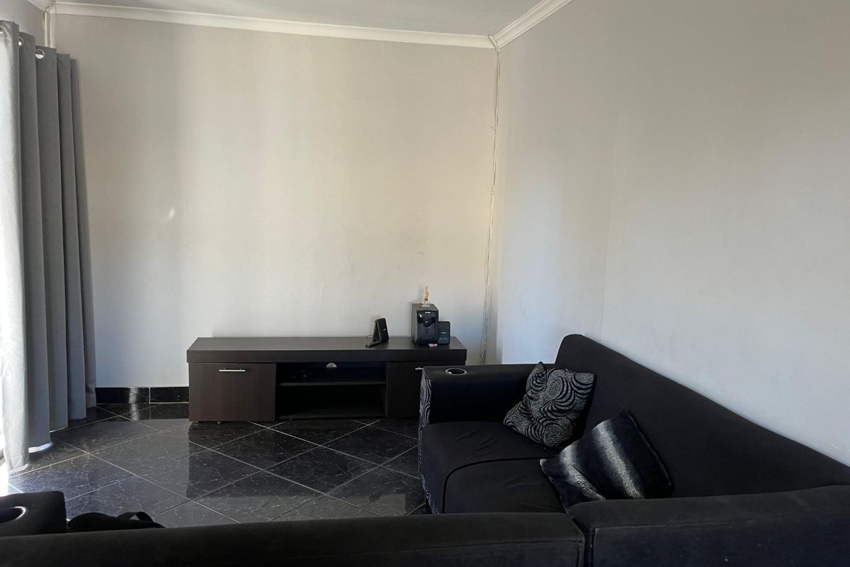 A living room featuring dark tiled flooring, neutral walls, and a sliding door with curtains, providing a functional and well-lit space.