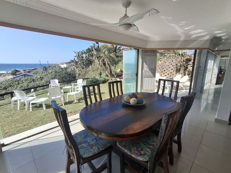 Open-plan living area featuring large stacking glass doors that open to a coastal view, tiled flooring, and a ceiling fan.