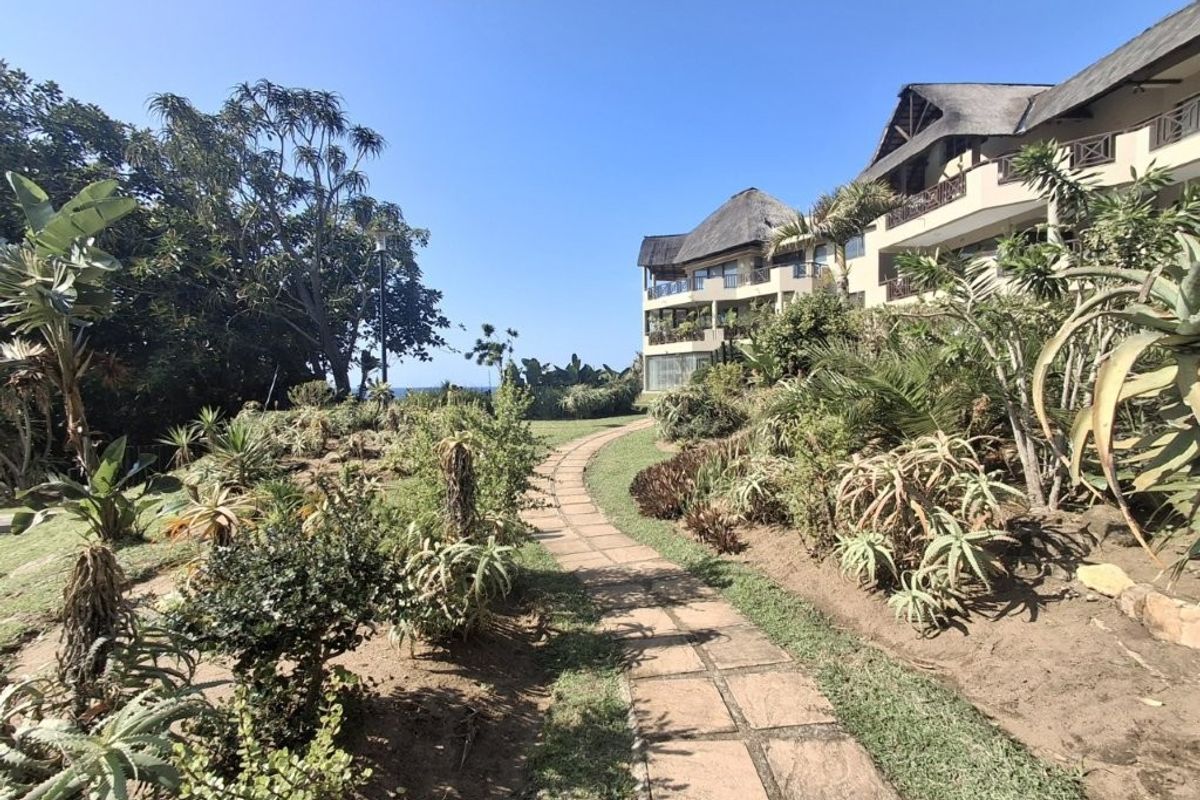 A view of the rear exterior of the apartment complex featuring a paved garden path and established landscaping leading towards the building.