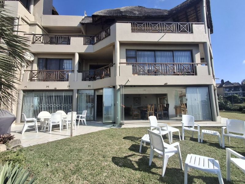 Rear view of a multi-story apartment building featuring multiple balconies, sliding glass doors, a tiled patio area, and a private lawn.
