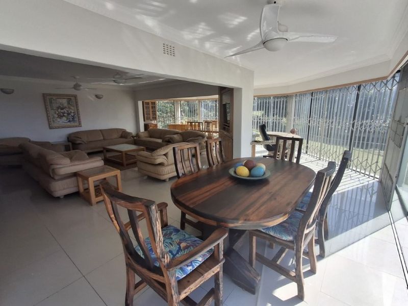 Spacious open-plan living and dining area featuring tiled floors, ceiling fans, and large sliding glass doors with security gates leading to the exterior.