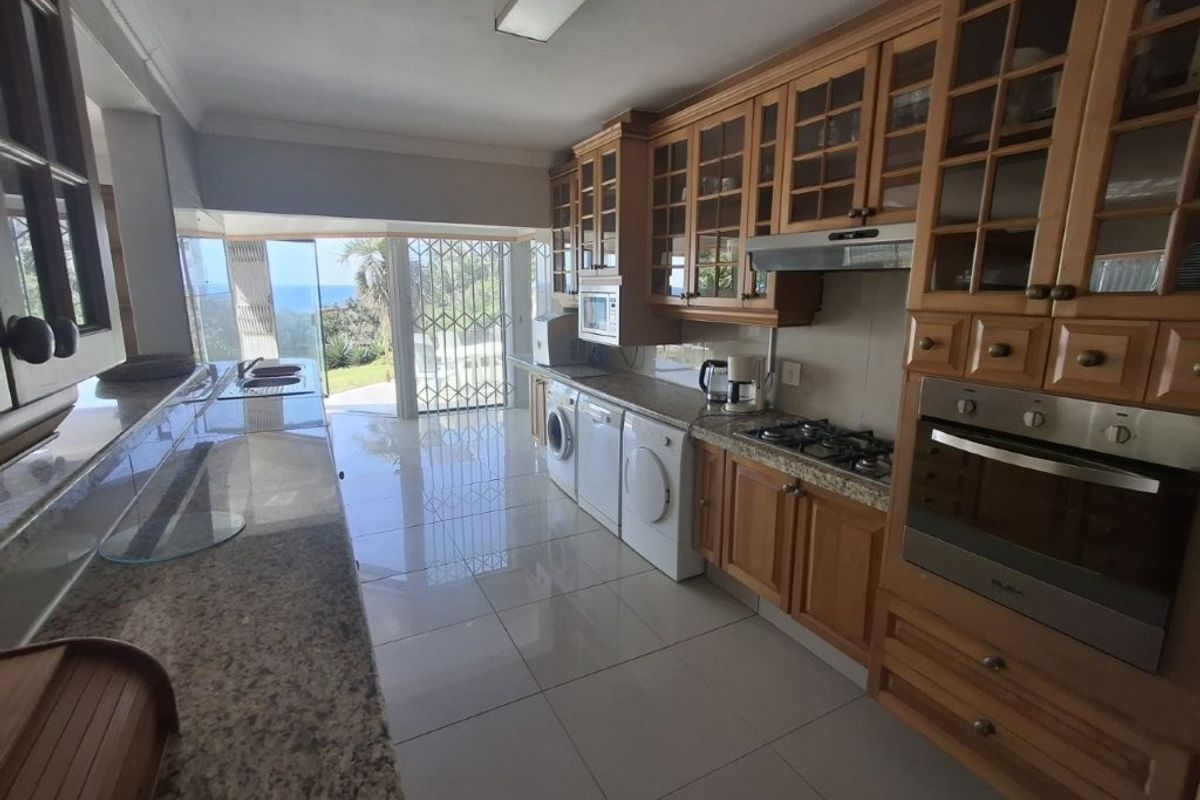 Spacious kitchen featuring granite countertops, ample wooden cabinetry, built-in oven and gas hob, with direct access to a patio area and ocean views.