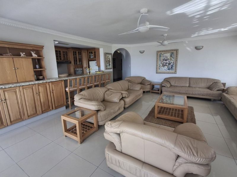 Spacious open-plan living area featuring tiled floors, ceiling fans, and a built-in kitchen bar with granite countertops and wooden cabinetry.